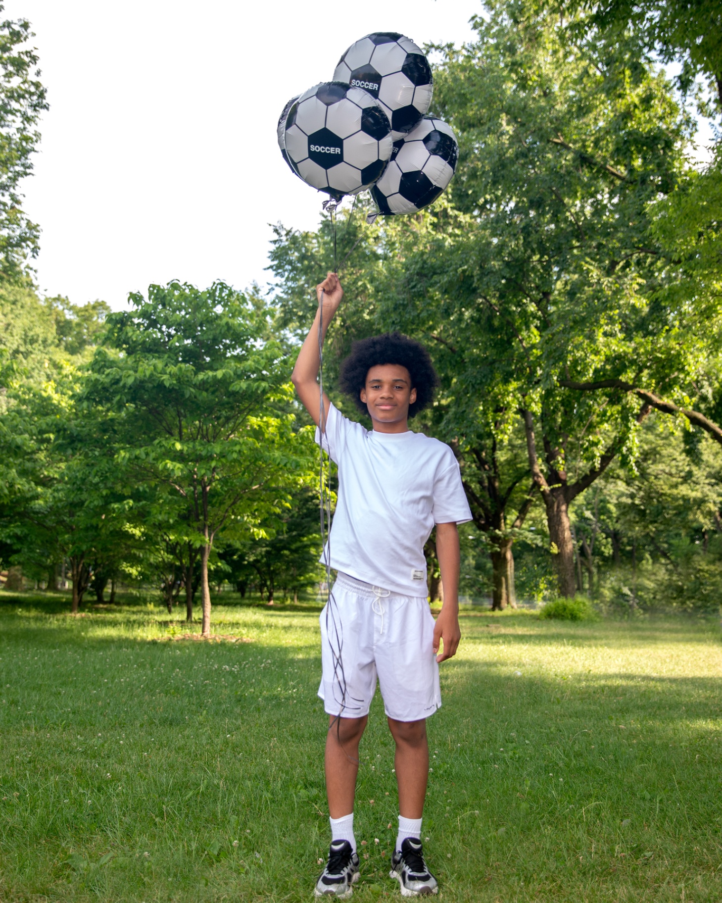 Boy in all-white fit holding three SOCCER balloons