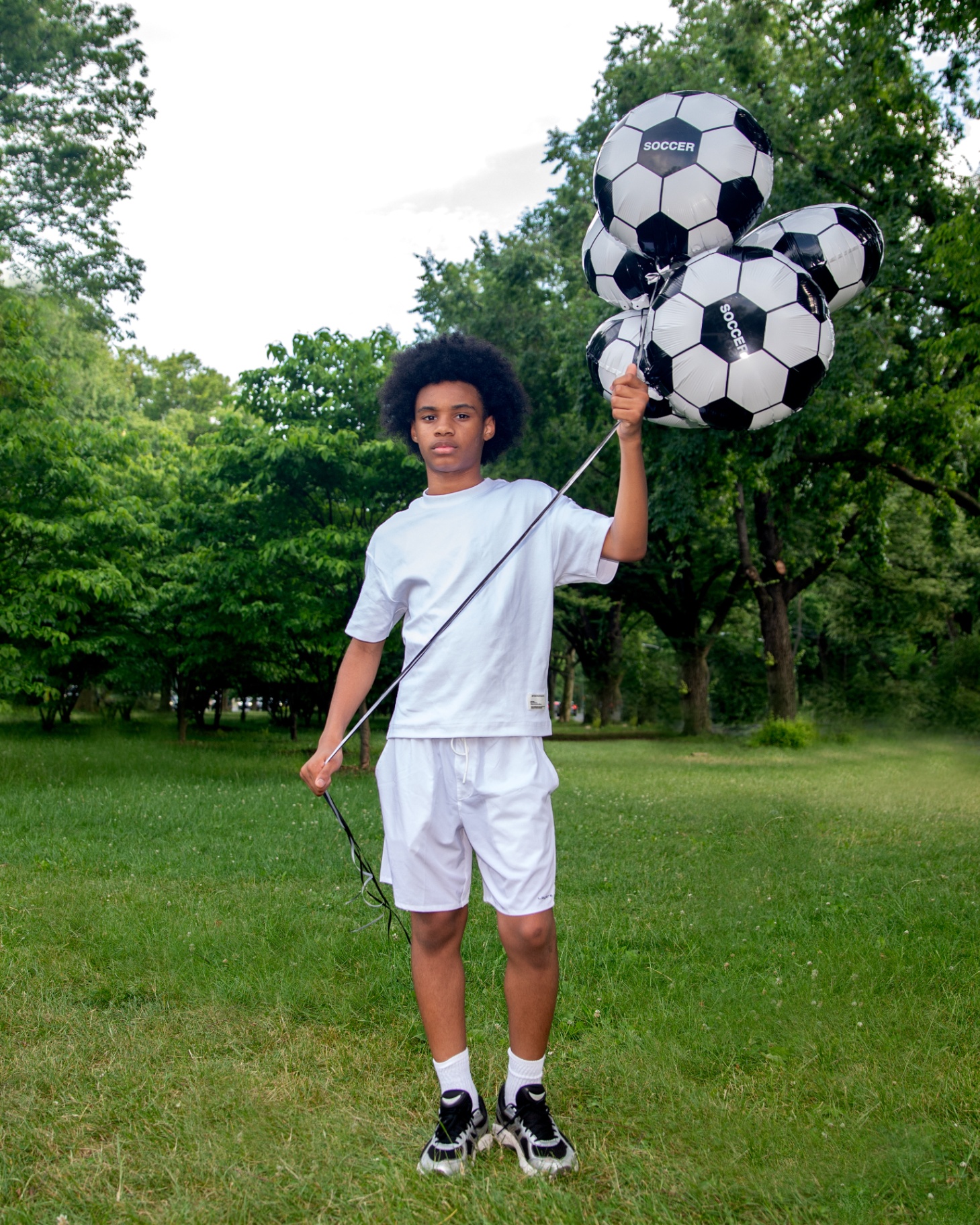 Teen in all-white holding a bunch of SourAppleBXNYC soccer-ball balloons